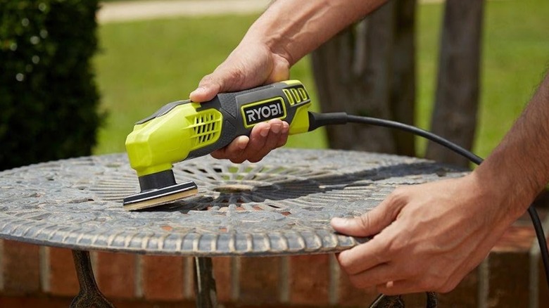 A person using a Ryobi detail sander on an outdoor table