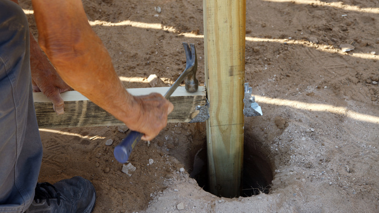 man hammering fence post into deep hole