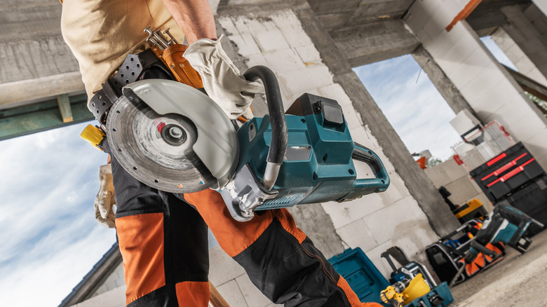 Construction Worker with a Professional Circular Saw in His Hand Walking Along Construction Site