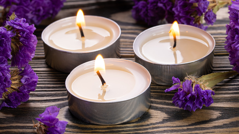 Three tea light candles surrounded by purple flowers