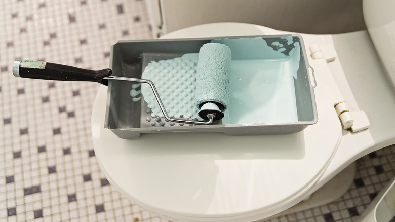 a paint pan and roller with light blue paint sits on a white toilet