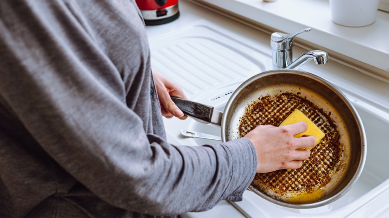 Person cleaning a burnt pan in the sink with a sponge