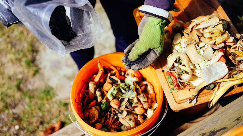 A person sprinkles material over food scraps in a bucket