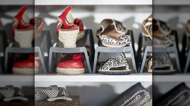 Shoes in organizer sit on the top shelf of a shoe cabinet while the bottom shelf has other items.