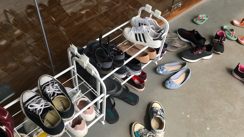 Shoes strewn across the floor of a home's entryway or placed messily in a flimsy shoe shelf.