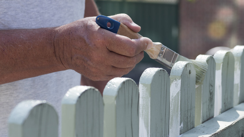 A man's hand painting a fence with rounded pickets