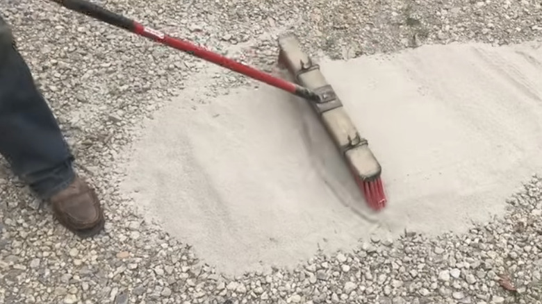 Man brushing concrete mix into gravel driveway