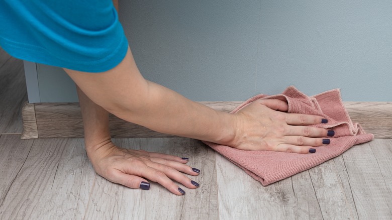 woman wipes baseboard with cloth