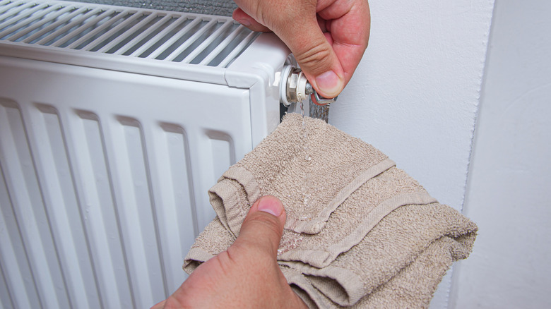 A person bleeds their radiator while holding a wash cloth underneath