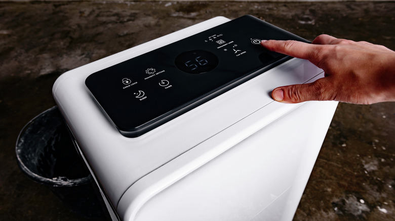 A woman's hand turns on a dehumidifier in a wet crawl space