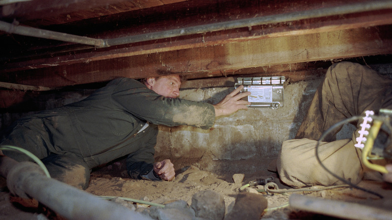 Two men do repairs in a dark crawl space