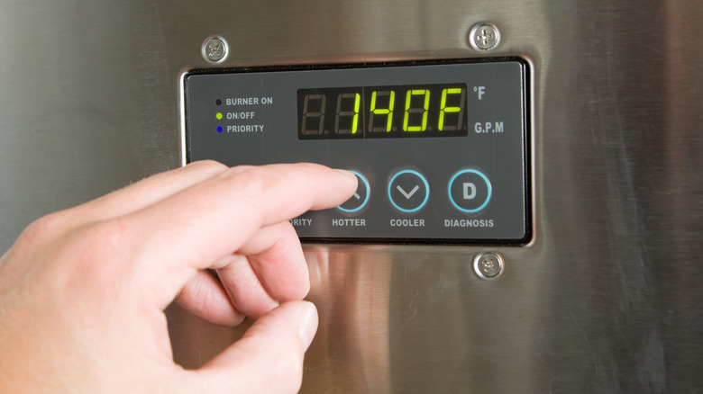 A hand setting the temperature on a tankless water heater control panel