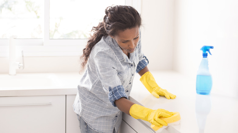 Woman wearing gloves scrubbing a countertop with a sponge