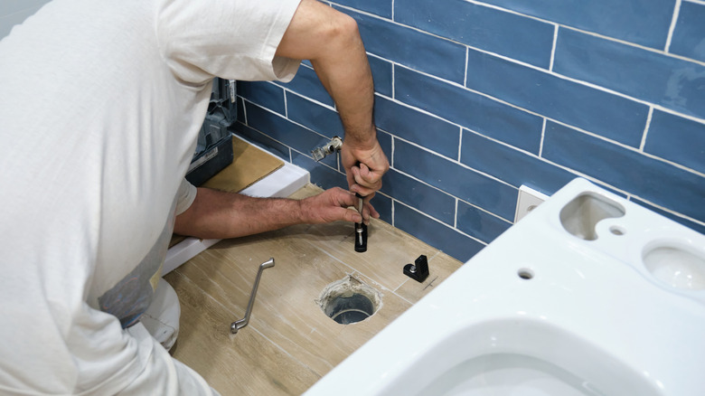 Person installing a toilet into a wood tile floor