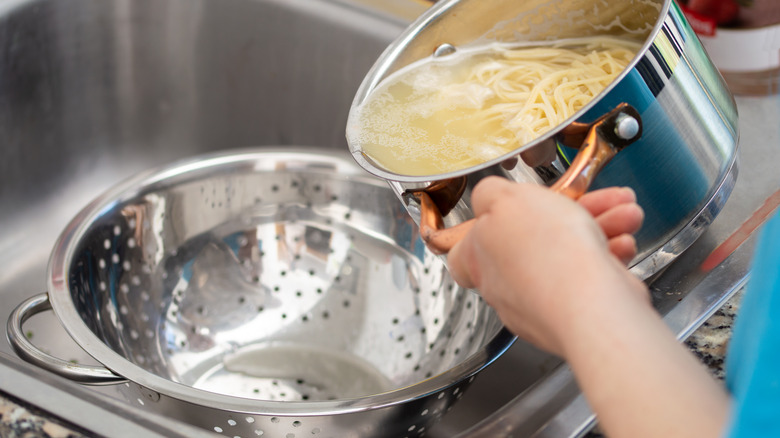 Person draining pasta in colander 