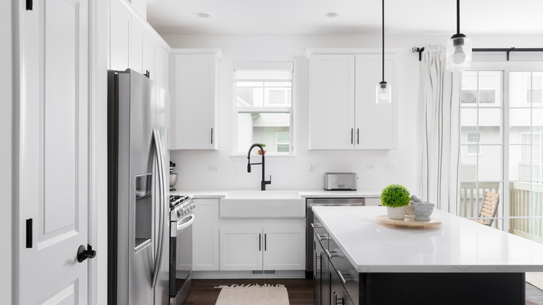 A mostly white kitchen with a white sink, black faucet, and stainless steel appliances