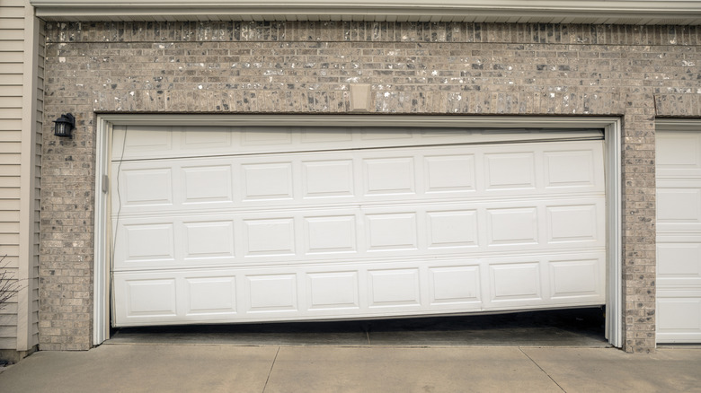 Crooked white garage door with gap between the door and the ground.