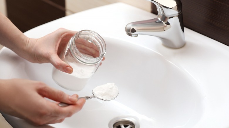 Person holding baking soda in spoon in sink