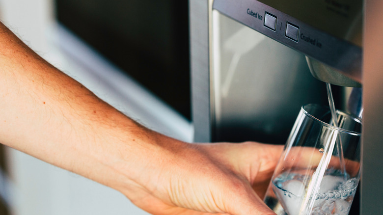 Hand filling glass from a fridge water dispenser