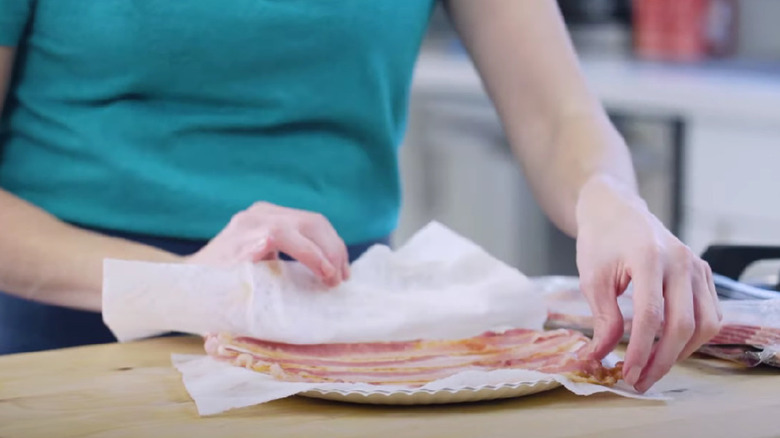 Hands setting paper towels over bacon