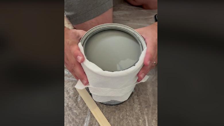 Hands holding wrapping paper towels around paint can