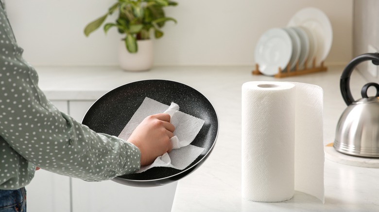 Hand cleaning a pan with a paper towel