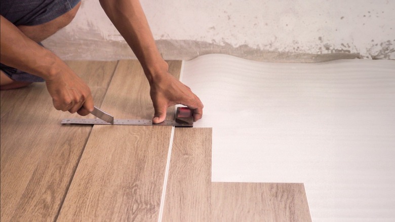 Man cutting vinyl flooring plank during installation over moisture barrier