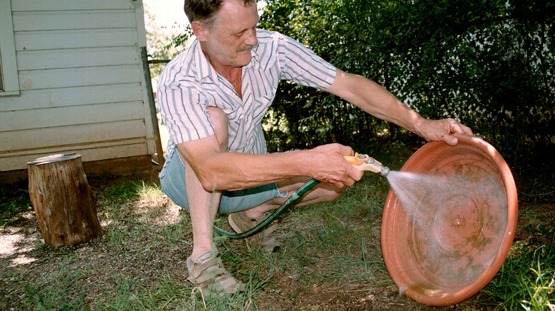 A man is using a hose to clean a birdbath.