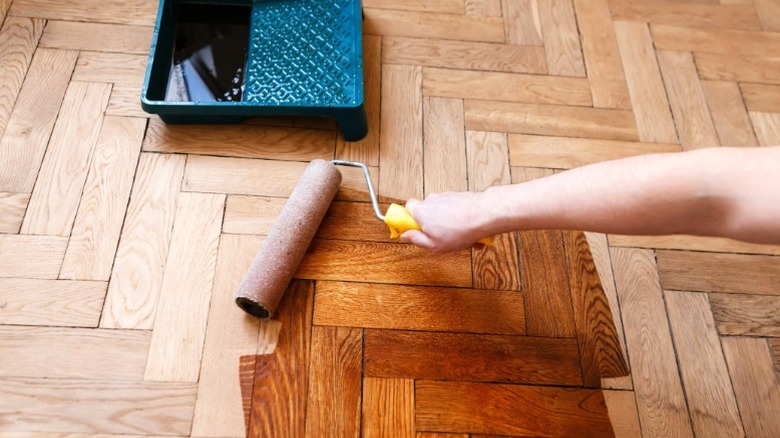 Person applying finish to parquet wood floor with roller and paint tray