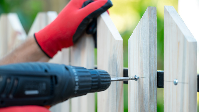 Person repairing a wood fence with new slats