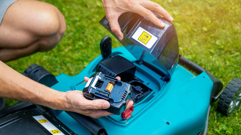 A person replacing a lawnmower battery