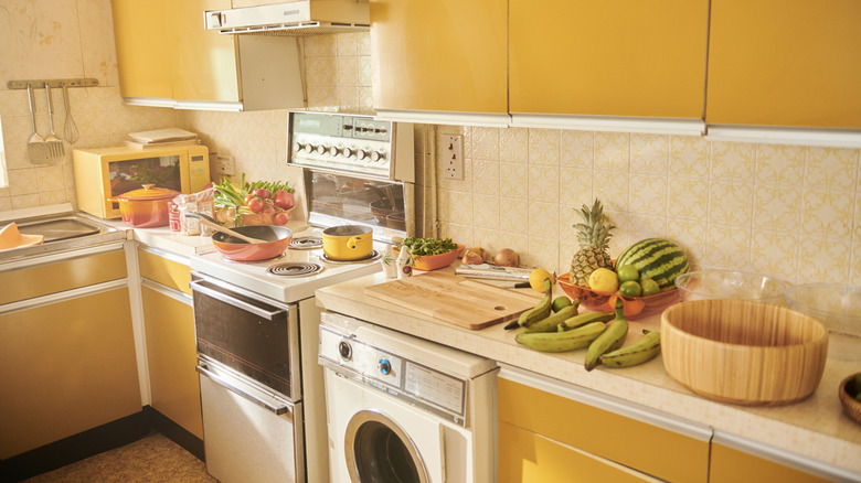 A kitchen counter is crowded with appliances and food.