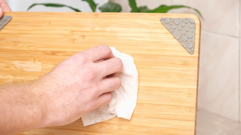 person sealing wooden cutting board with paper