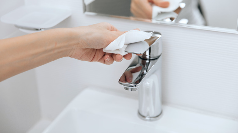 person cleaning faucet with paper