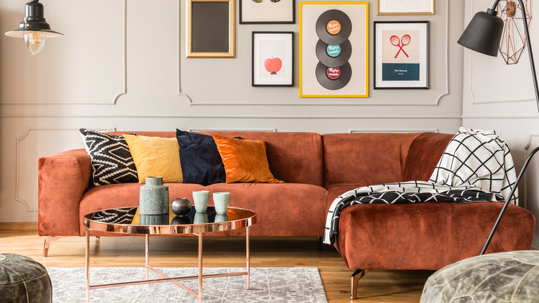 Living room with a dark orange velvet couch and gray velvet ottomans