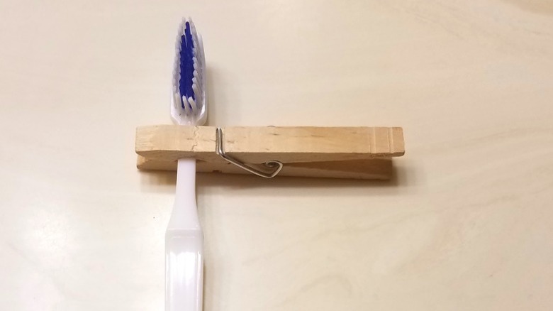 Wooden clothespin holding toothbrush on wood cabinet door