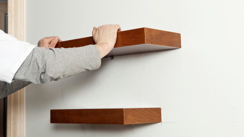 Person installing wooden shelves on white wall