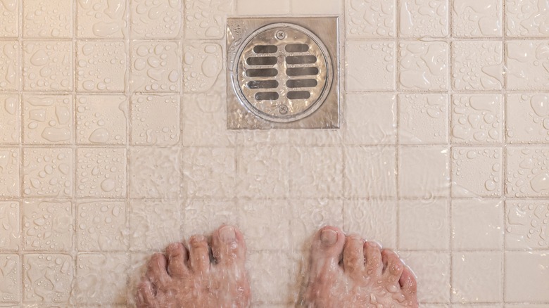 Close-up of shower drain and a pair of feet