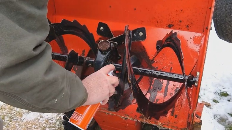 Man's hand spraying silicone lubricant on snow blower augers