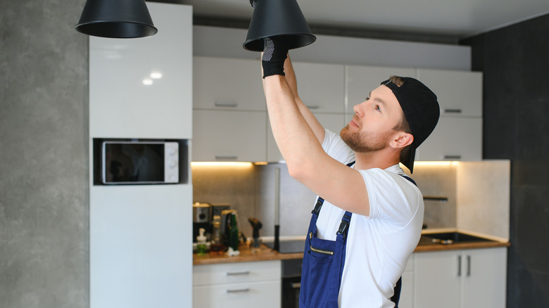 A man changes the bulb in a pendant light in the kitchen.