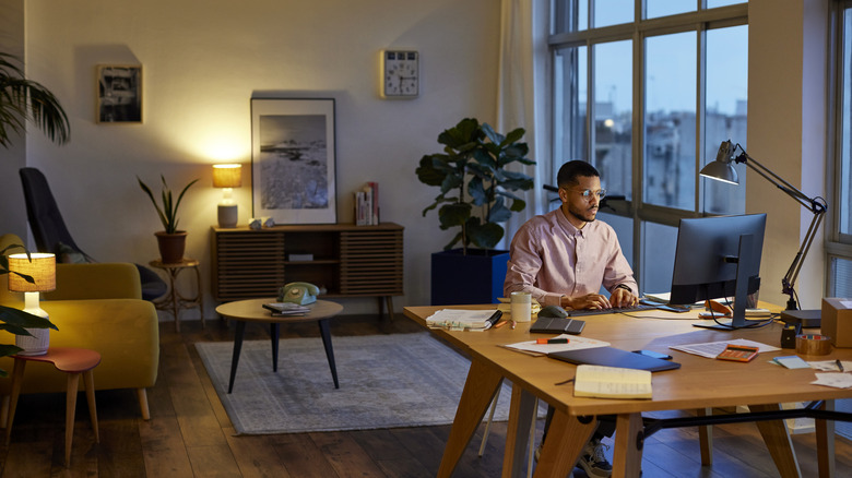 A man works from home at a desk in his lounge in the early evening.