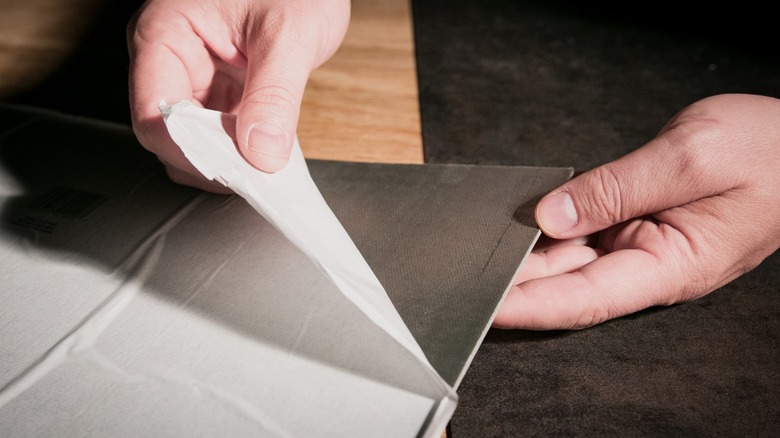 Person removing paper backing from black peel-and-stick floor tile