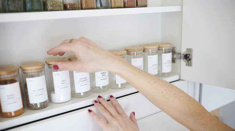 Hands reaching for spices in a white cupboard