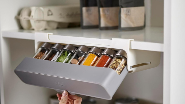 Person opening an under-cabinet spice organization system holding seven different spice bottles