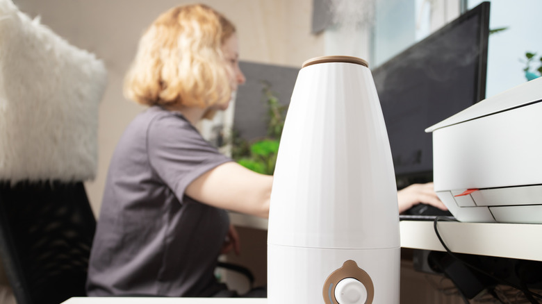 A woman sits by a computer while using a humidifier