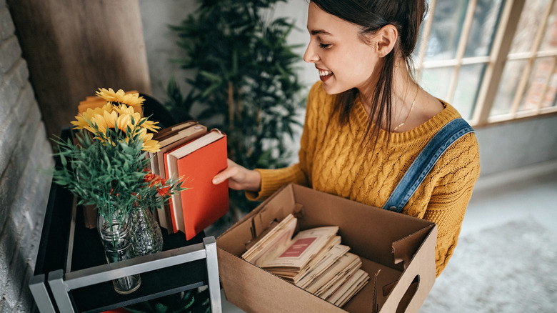 A young woman organizing books from a box on a bookshelf.