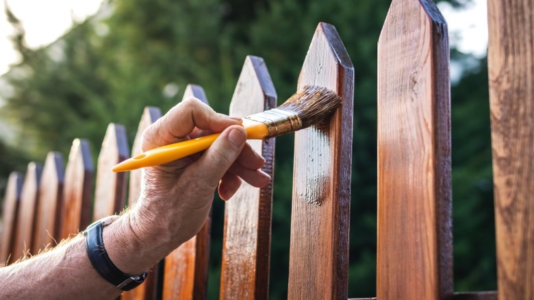 A person brushes sealant or stain on a wood fence to protect it