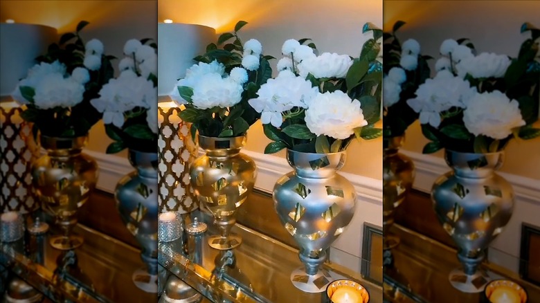 Spray painted apothecary jars serve as vases for white flowers on a glass table.