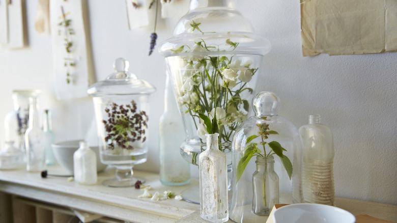 Apothecary jars with flowers inside on a side table.