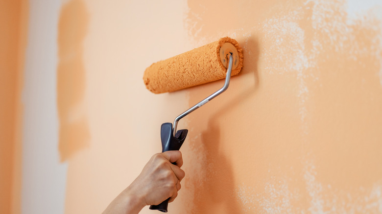 Hand of person painting a wall orange with a paint roller